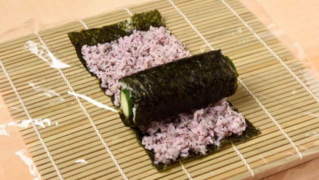 紫の酢飯の上にきゅうりの巻き寿司をのせて巻く
